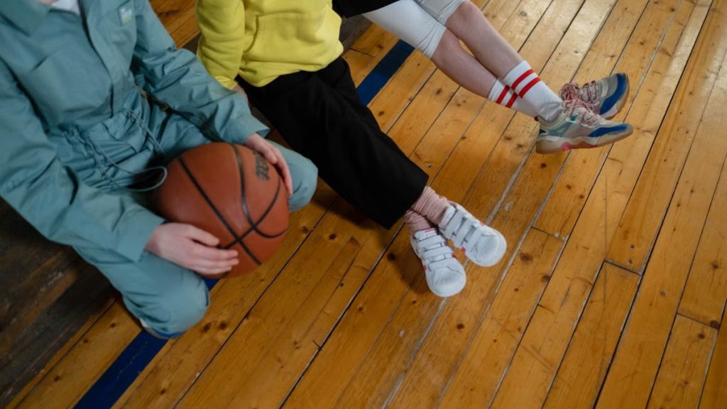 Two people sitting on a wooden gym floor holding a basketball, showcasing leisure and sportswear.